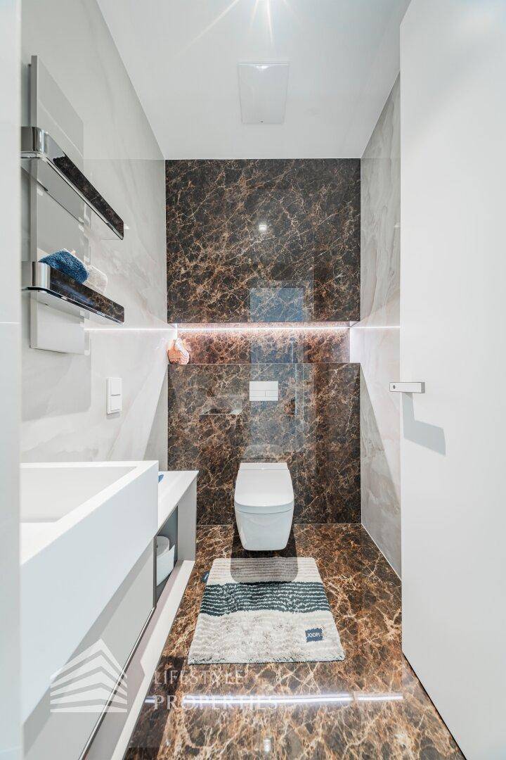 Elegantes Gäste-WC mit dunklen Marmorfliesen, modernem Waschtisch und indirekter Beleuchtung.
