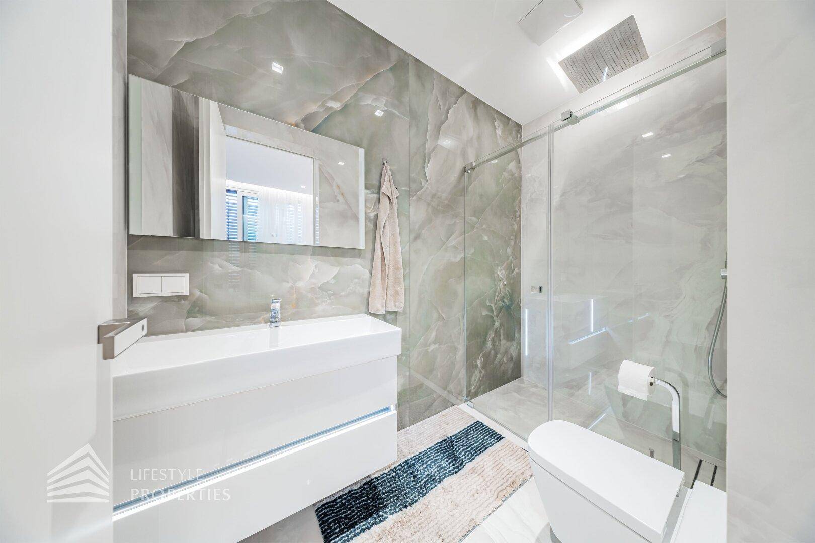 Helles Badezimmer mit modernen Armaturen, Marmorfliesen und wandhängendem WC.
