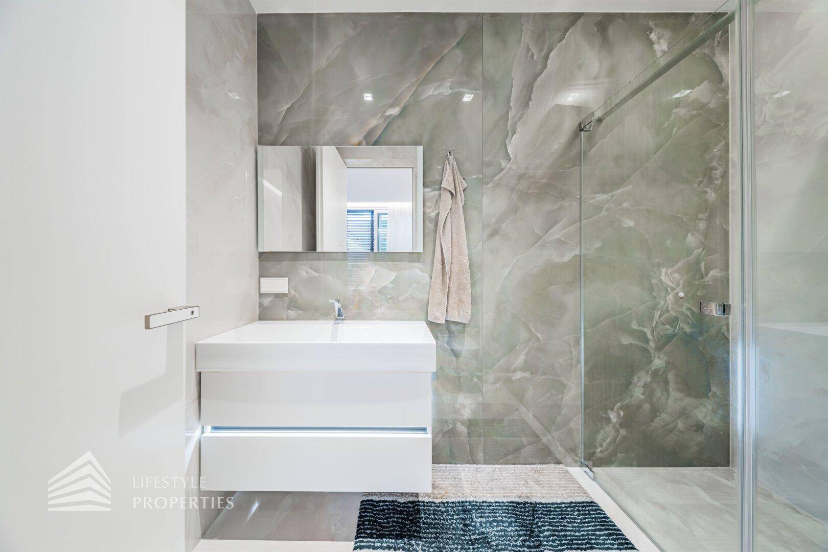 Modernes Badezimmer mit grauen Marmorfliesen, schwebendem Waschtisch und ebenerdiger Dusche.