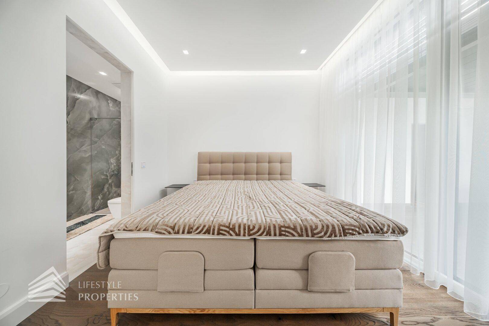 Komfortables Schlafzimmer mit Doppelbett, Holzboden und direktem Zugang zum modernen Badezimmer.