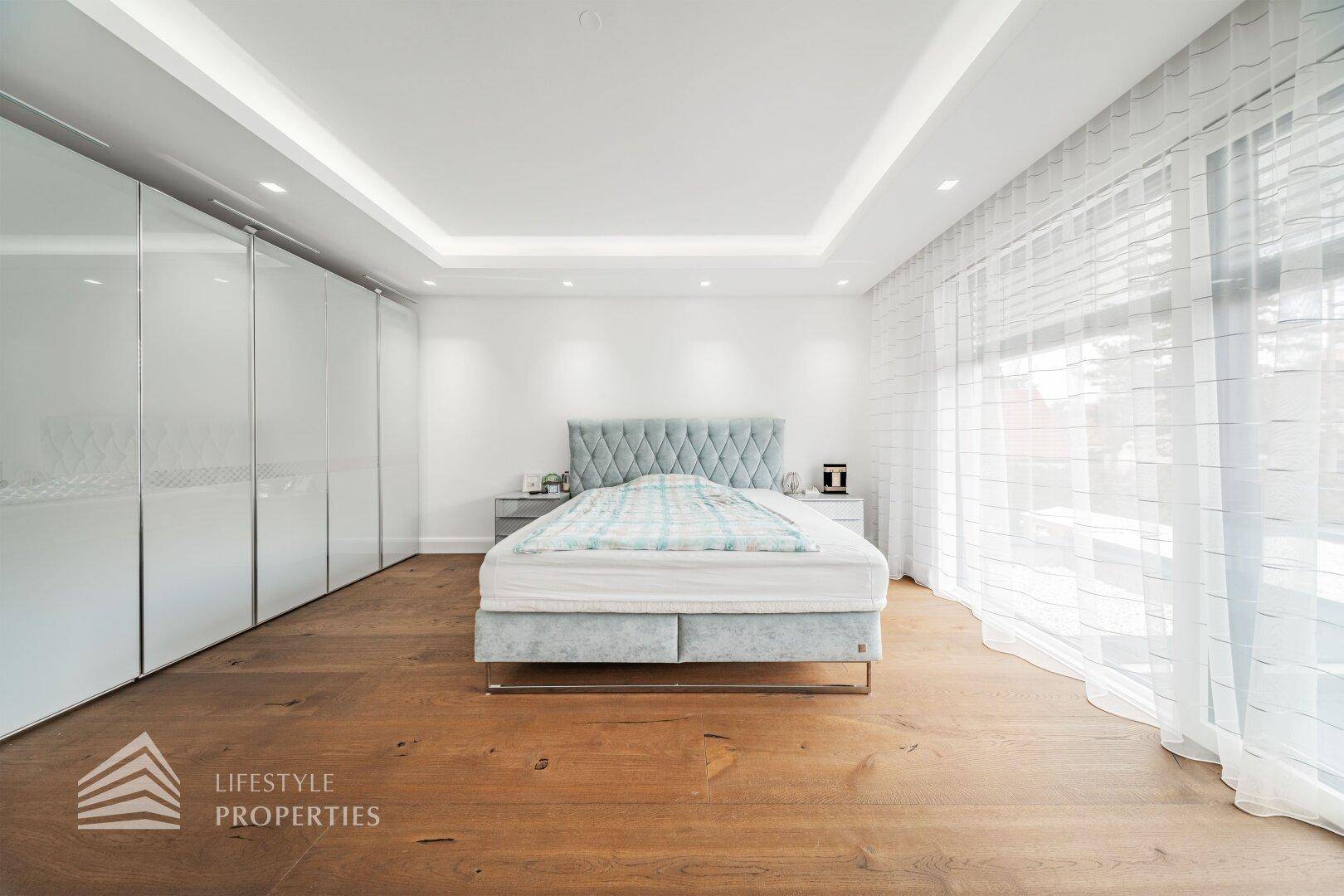 Elegantes Schlafzimmer mit Doppelbett, Einbauschränken und Holzboden in heller Atmosphäre.