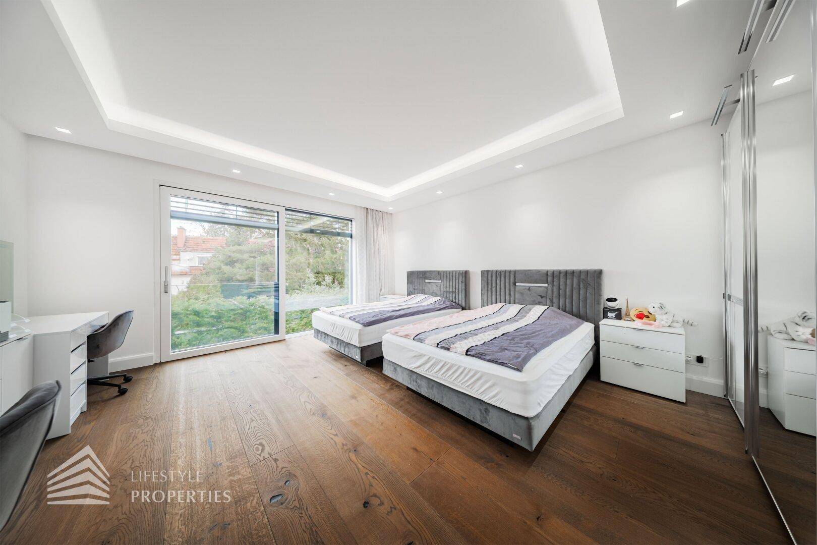 Helles Schlafzimmer mit zwei Einzelbetten, Holzboden und großem Fenster mit Zugang zum Balkon.