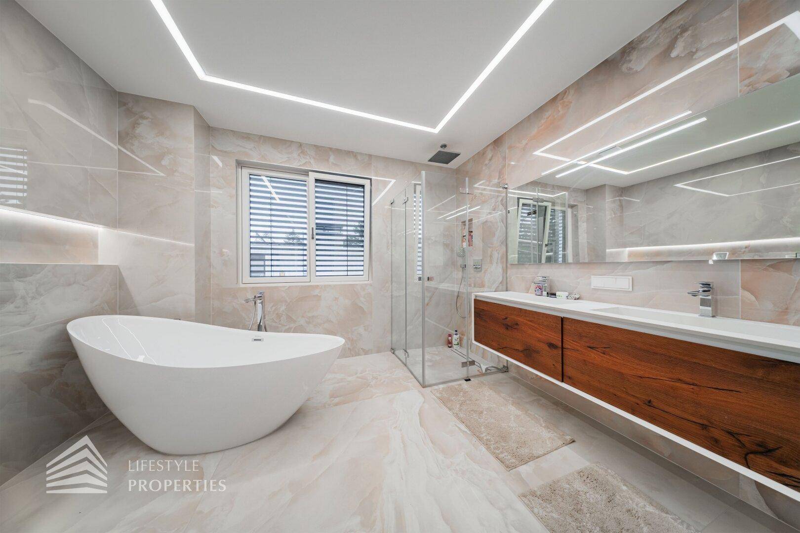 Modernes Badezimmer mit freistehender Badewanne, Doppelwaschbecken und ebenerdiger Dusche in hellen Tönen.
