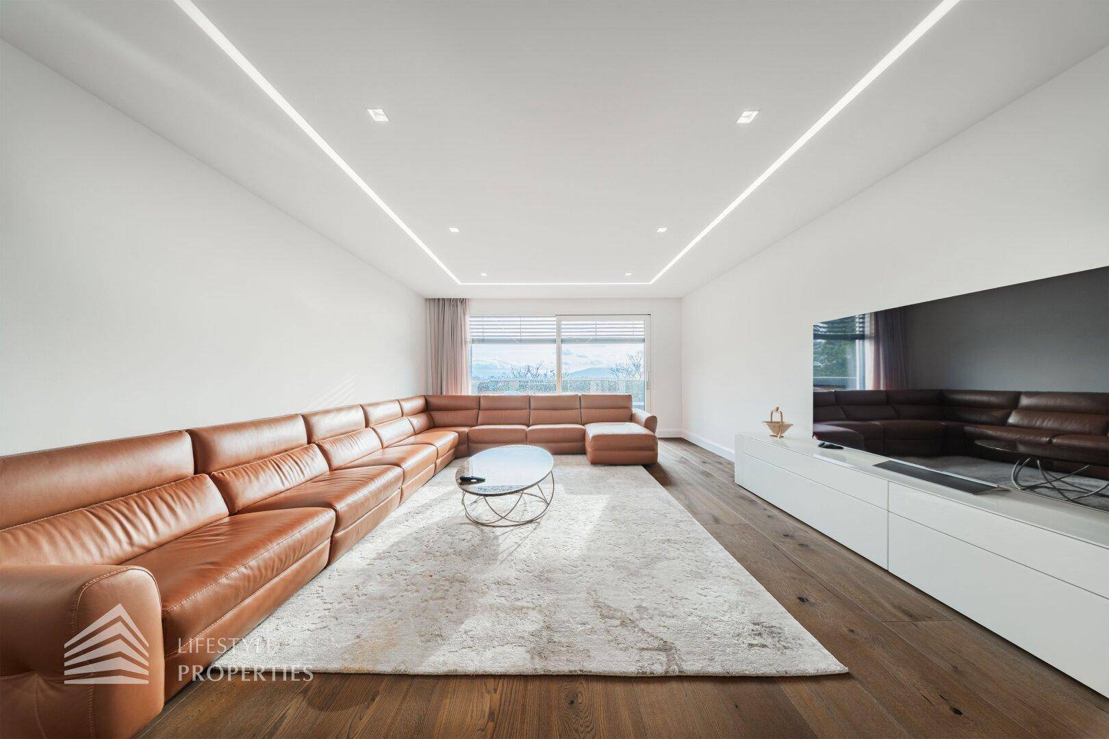 Geräumiges Wohnzimmer im Dachgeschoss mit großem Ledersofa, Holzboden und Blick nach draußen.