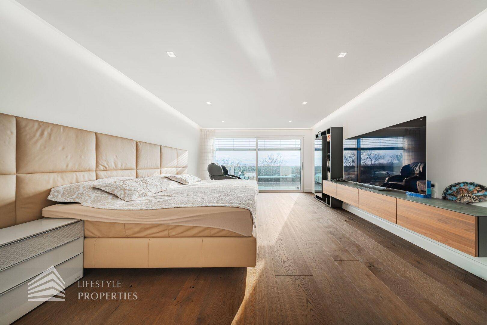 Großes Schlafzimmer im Dachgeschoss mit Doppelbett, Holzboden und breiter Fensterfront.