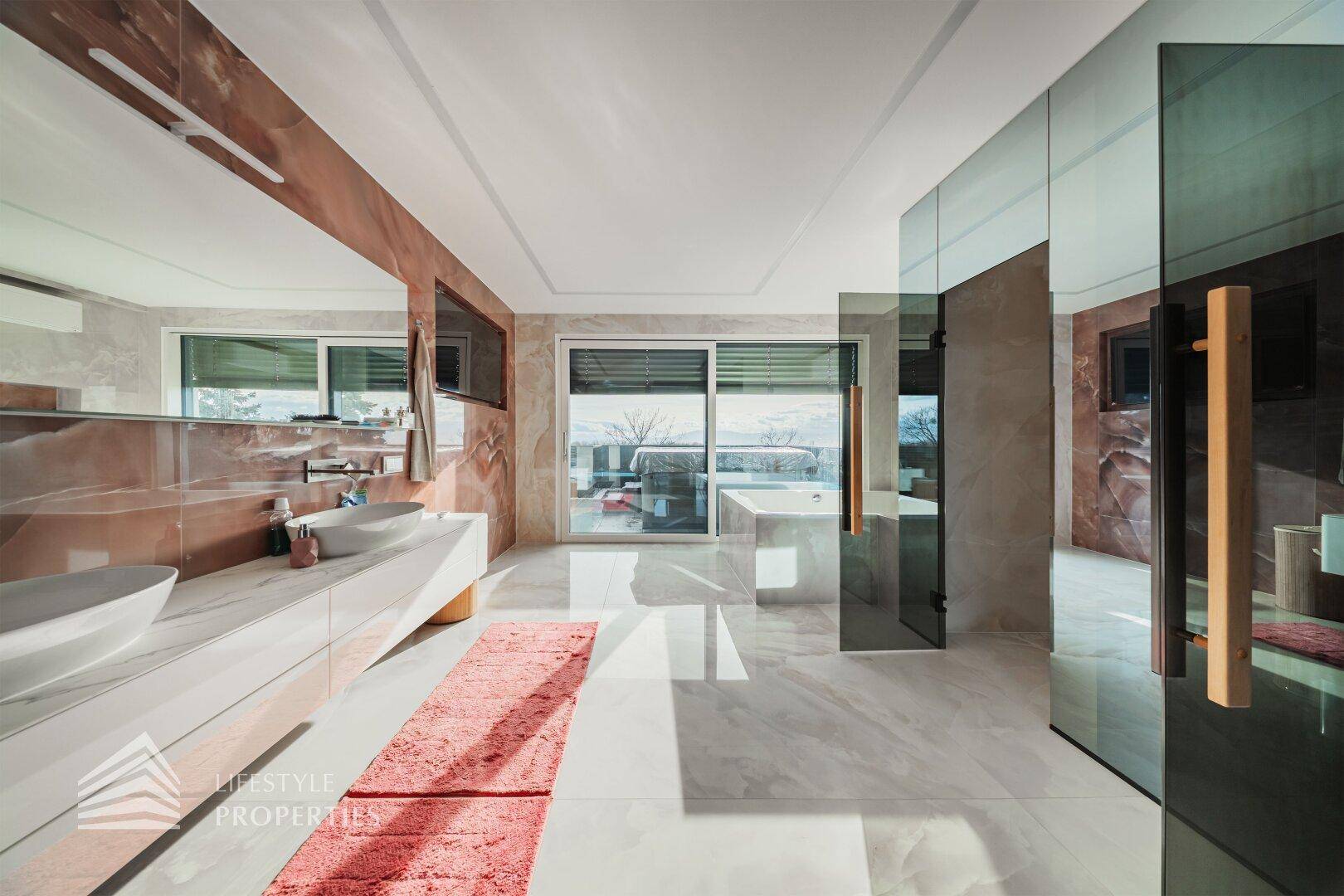 Elegantes Badezimmer mit Doppelwaschbecken, Marmorfliesen und Glaswänden, die den Raum öffnen.