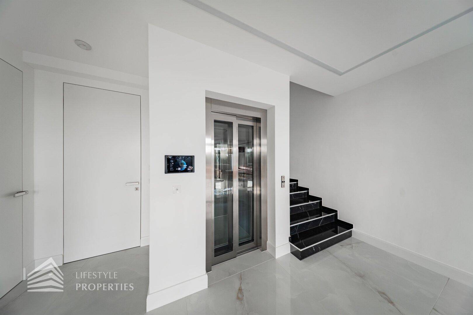 Heller Flur mit modernem Aufzug und Treppe, die die verschiedenen Ebenen des Hauses verbindet.