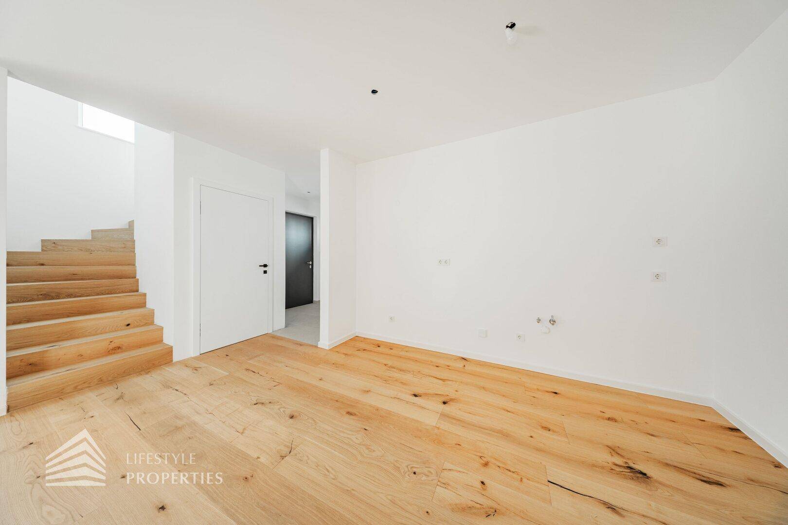 Geräumiger Wohnbereich mit hellem Holzboden und offener Treppe zum Obergeschoss.