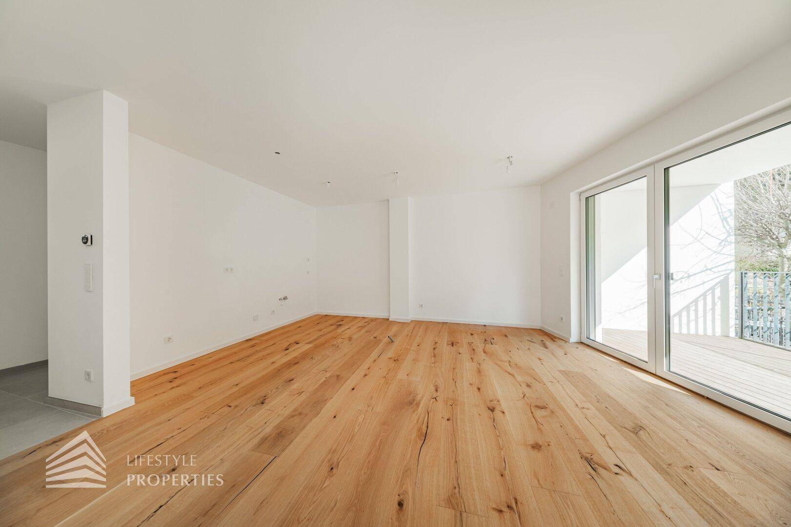 Geräumiger, heller Wohnbereich mit Holzdielenboden und Zugang zu einem Außenbereich.
