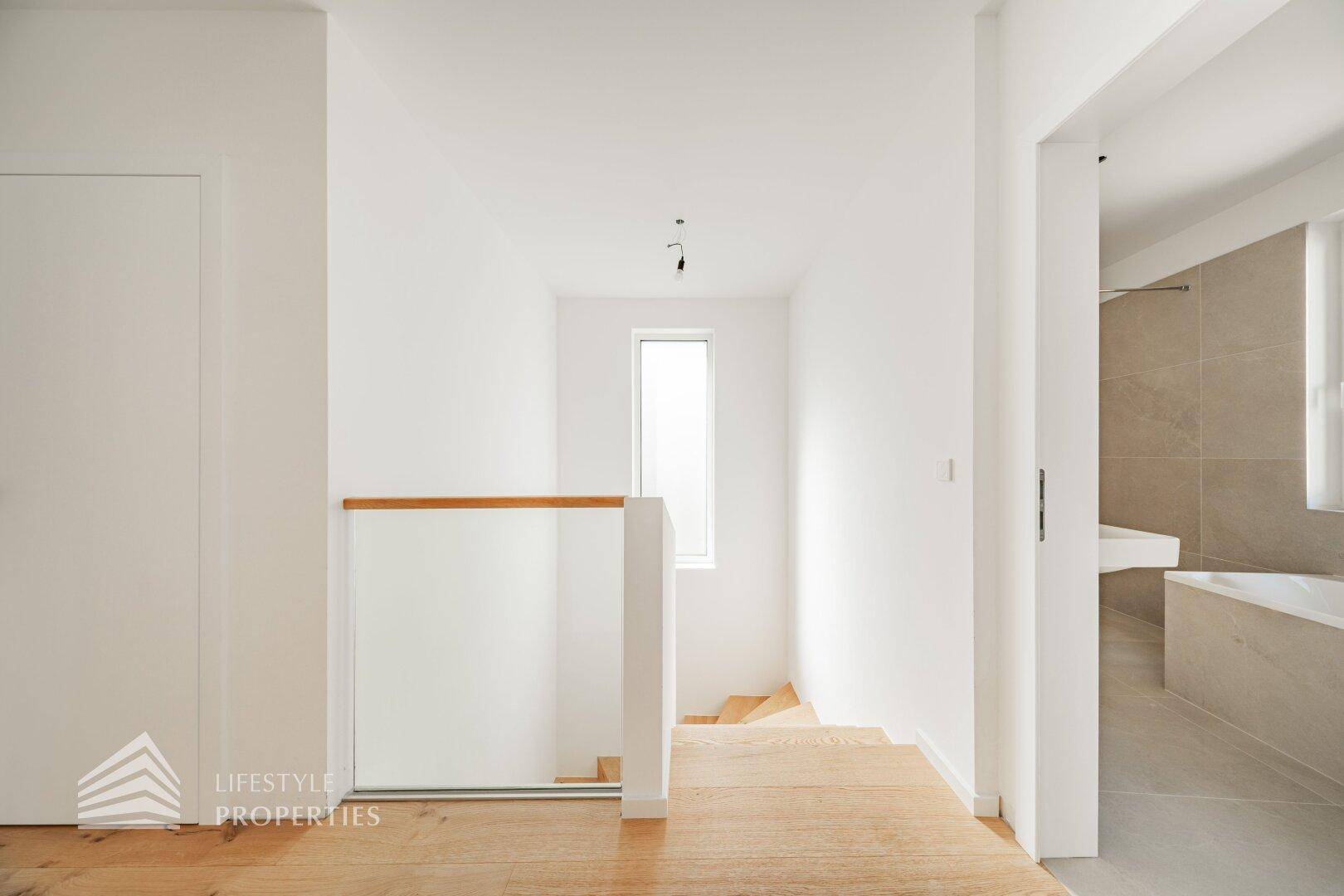 Heller Flur mit Holzdielenboden und minimalistischem Glasgeländer, das viel Licht durchlässt.