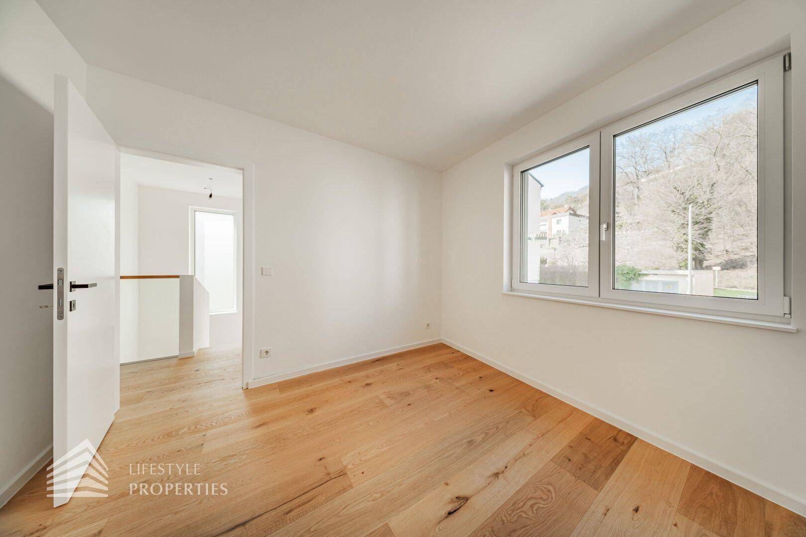 Geräumiges Schlafzimmer mit Holzdielenboden und Blick ins Grüne durch das Fenster.