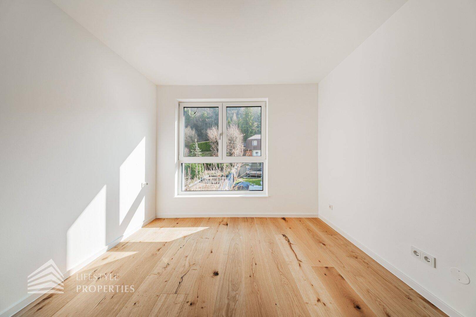 Helles Schlafzimmer mit Holzdielenboden und großem Fenster, das viel Tageslicht spendet.