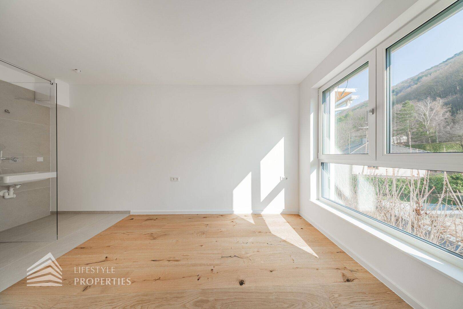 Modernes Schlafzimmer mit Holzdielenboden und integriertem Duschbereich mit Glaswand.
