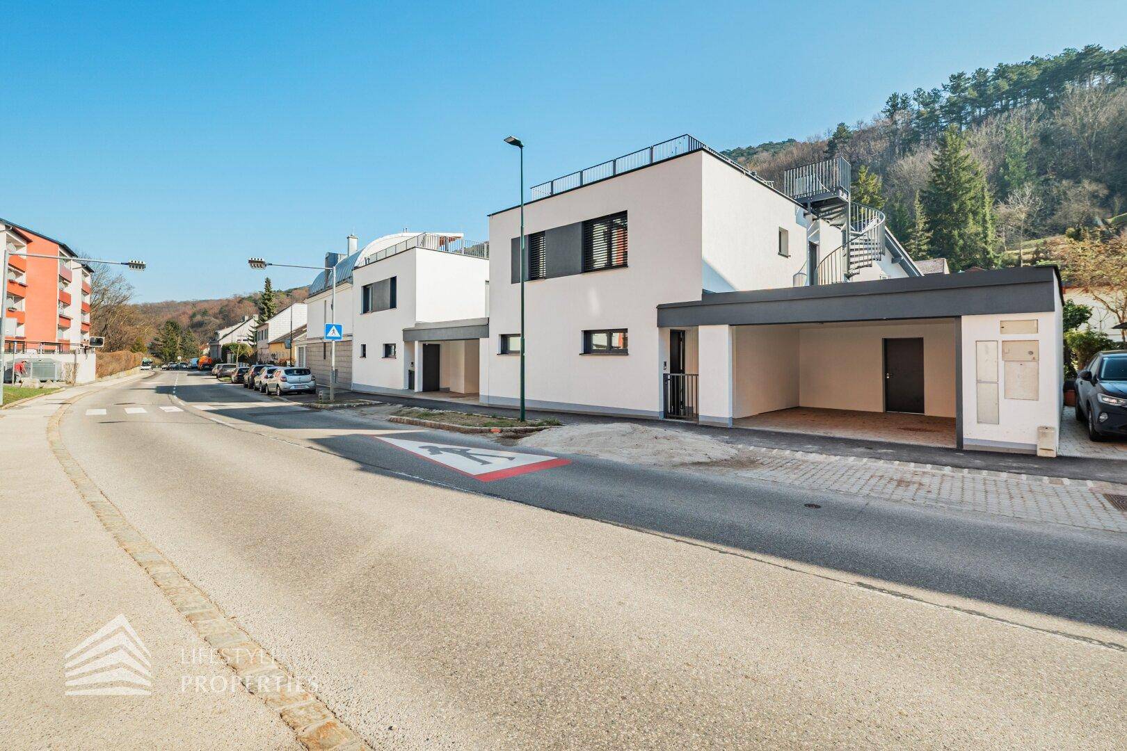 Moderne Gebäudeansicht mit weißer Fassade, Flachdach und externer Wendeltreppe zum Obergeschoss.