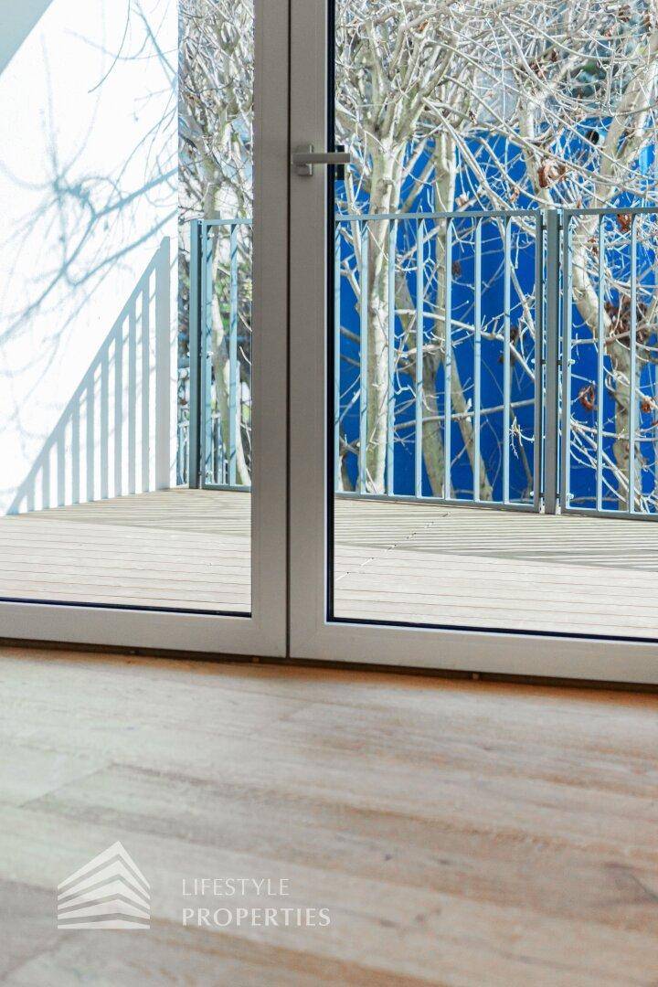 Glastür mit Zugang zu einem Holzdeck, umgeben von kahlen Bäumen und einem blauen Hintergrund.