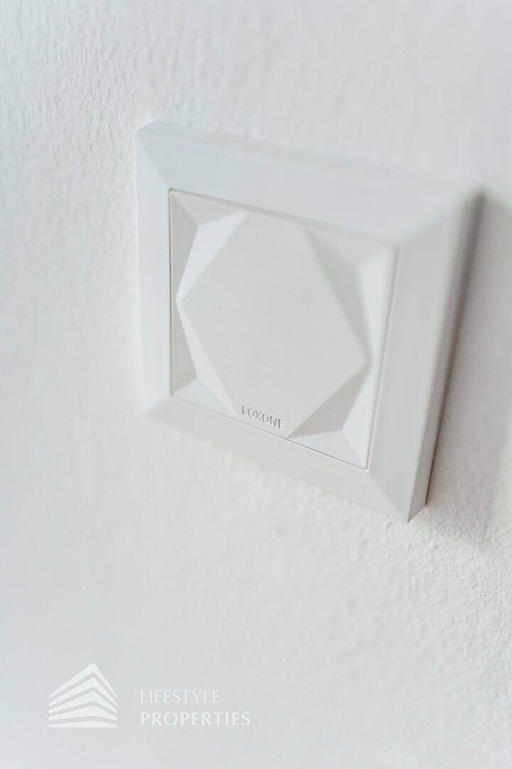 Moderner weißer Lichtschalter mit geometrischem Muster an einer hellen Wand.