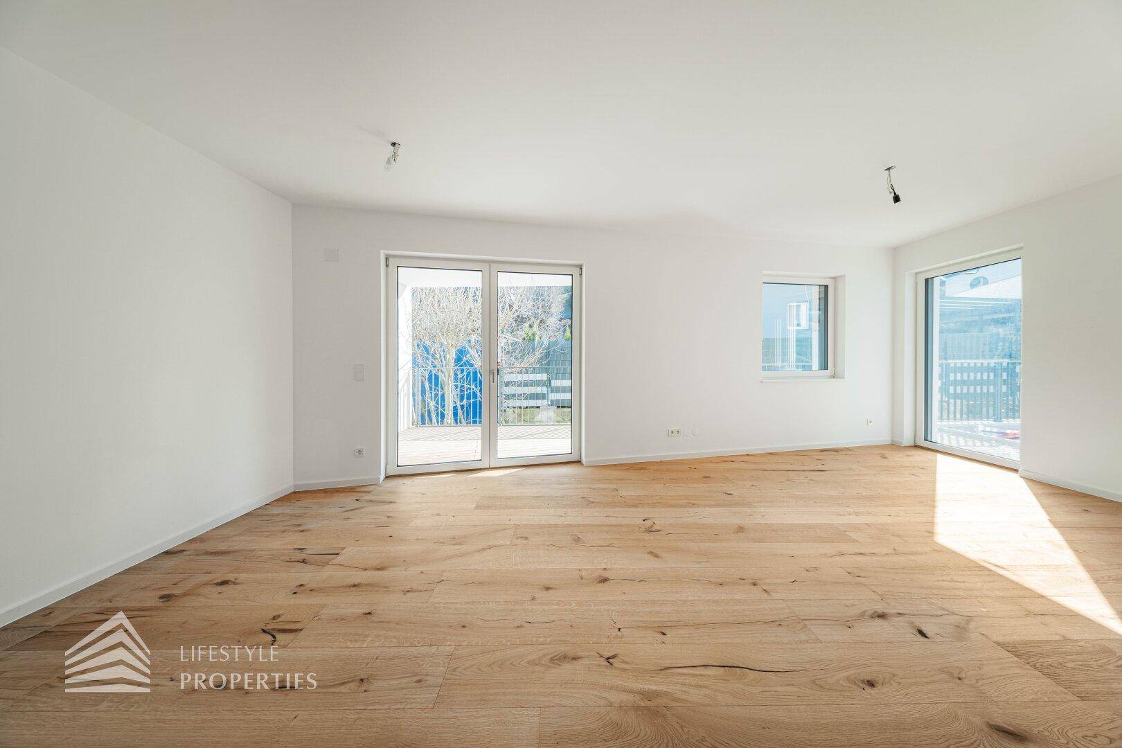 Geräumiger, leerer Wohnbereich mit hellem Holzboden und großen Schiebetüren zur Terrasse.