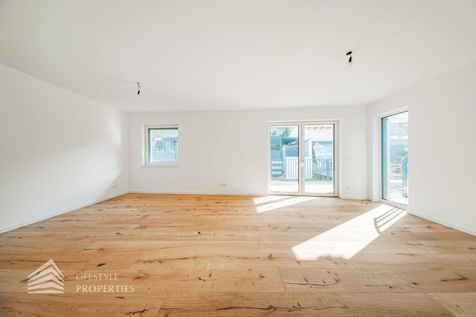 Lichtdurchflutetes Wohnzimmer mit breiten Holzdielen und großen Fenstern, die viel Tageslicht hereinlassen.