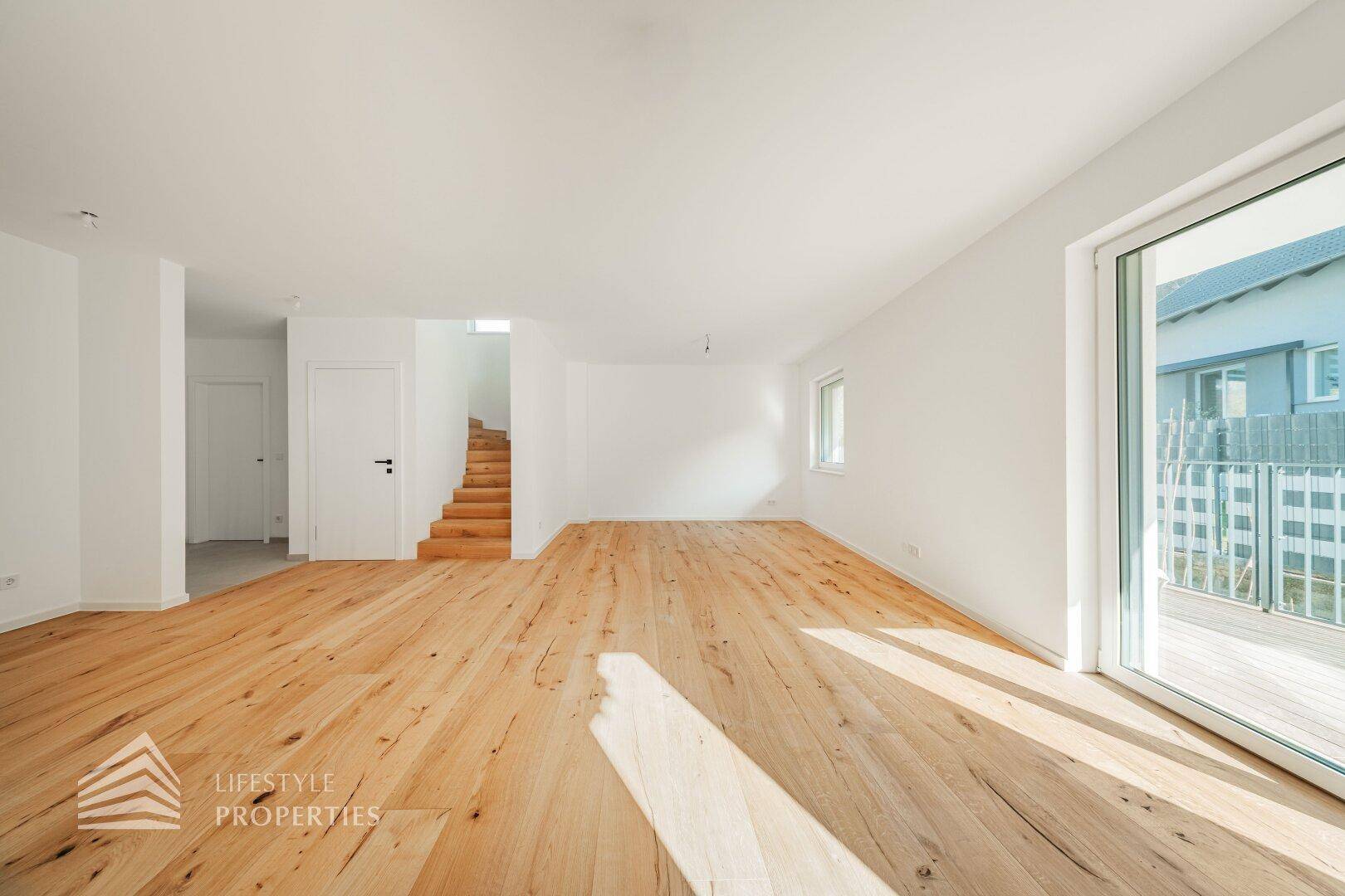 Großzügiges Wohnzimmer mit Holzboden und bodentiefen Fenstern, die Zugang zur Terrasse bieten.