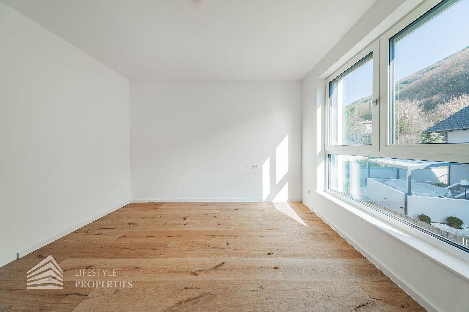 Helles Schlafzimmer mit Holzboden und großen Fenstern, die einen weiten Blick auf die Berge bieten.