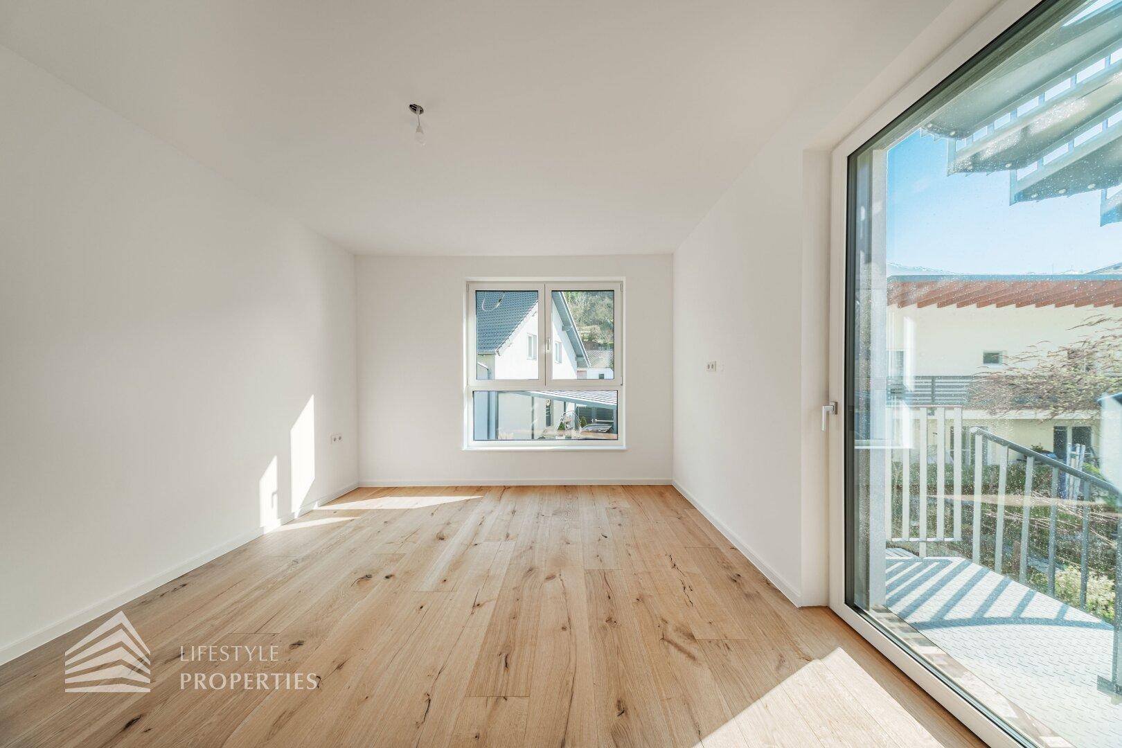 Helles, leeres Zimmer mit Holzboden und Zugang zu einem Balkon, ideal für individuelle Gestaltung.