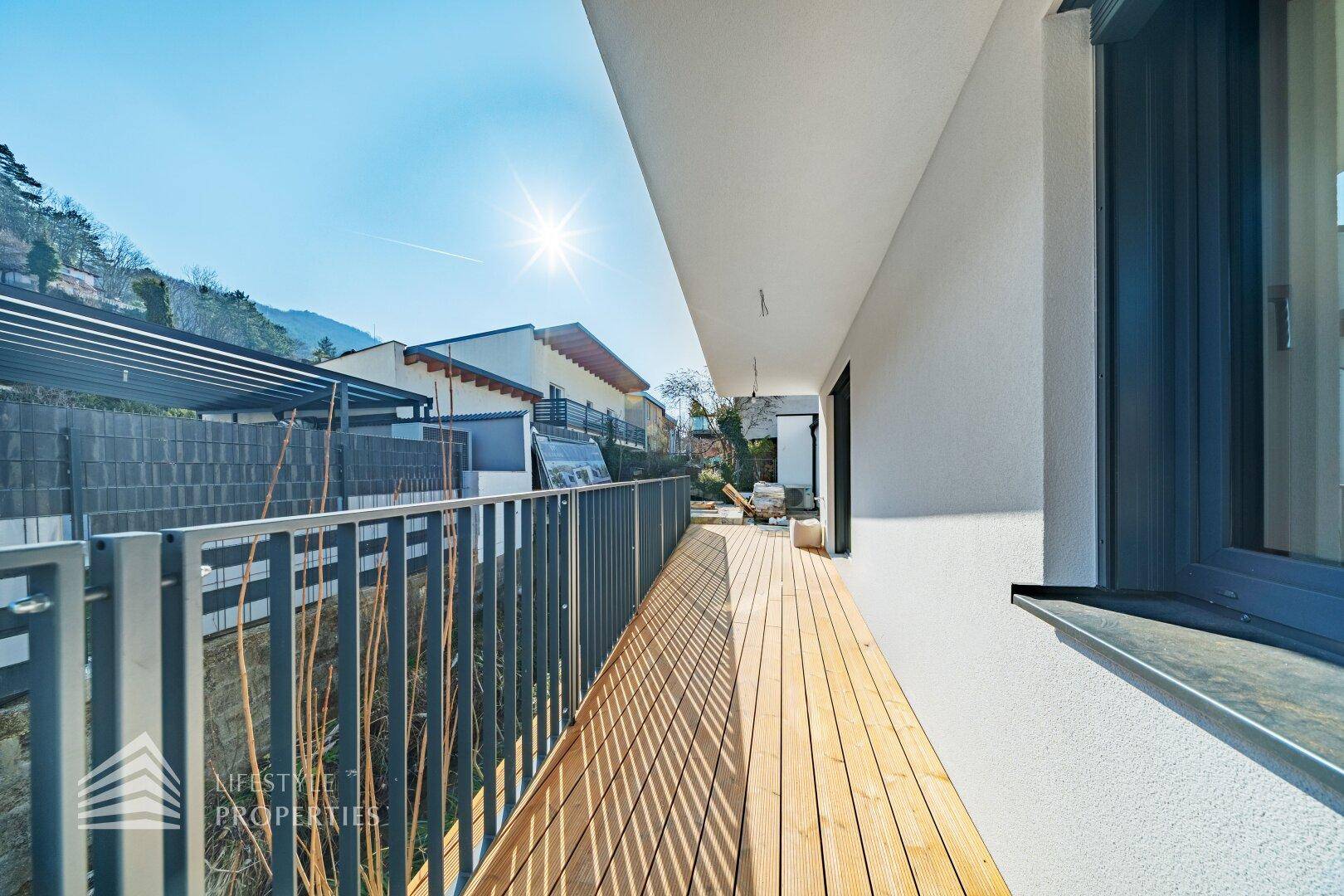 Sonniger Balkon mit Holzdielen und Metallgeländer, ideal zum Entspannen mit Blick auf die Hügel.