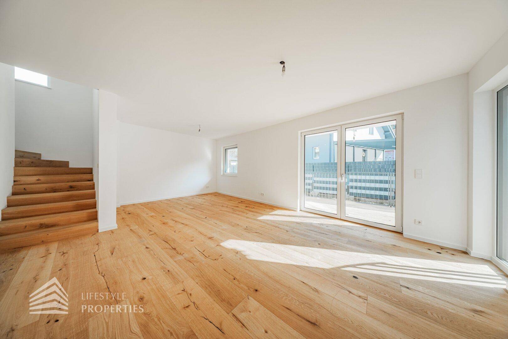 Helles, leeres Wohnzimmer mit breiten Holzdielen und Zugang zur Terrasse.