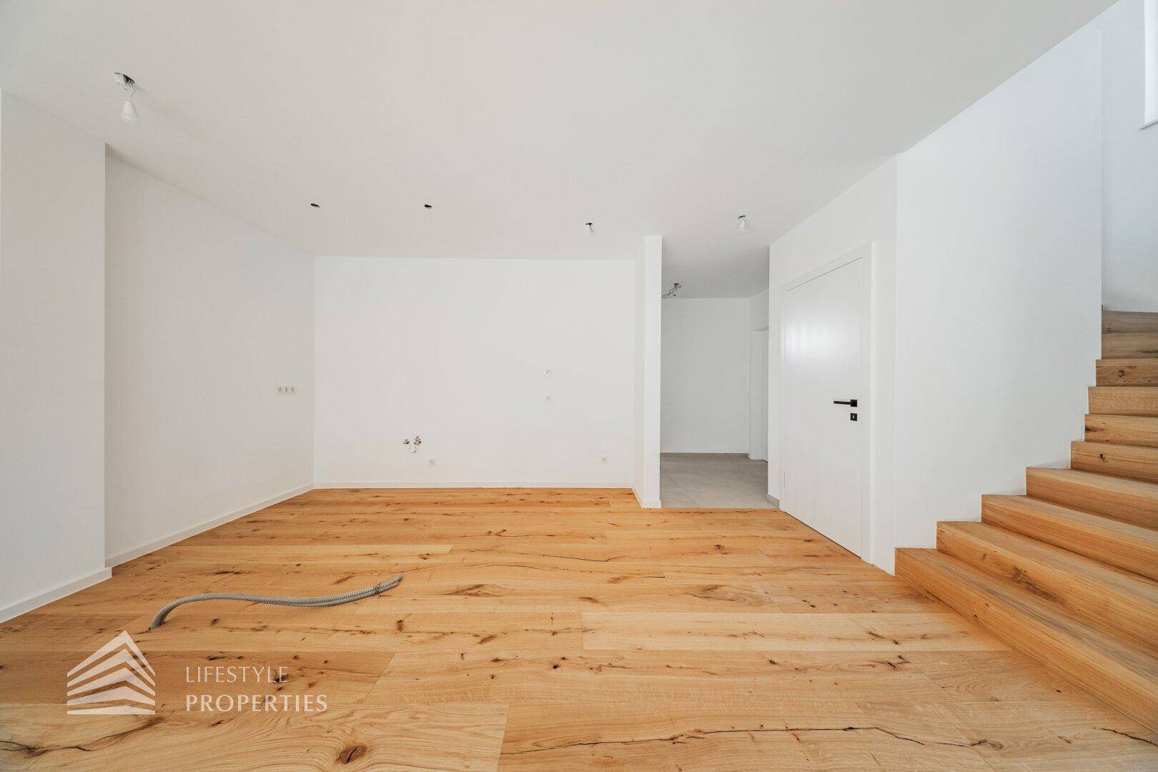 Geräumiges, leeres Wohnzimmer mit hellem Holzboden und weiß gestrichenen Wänden.