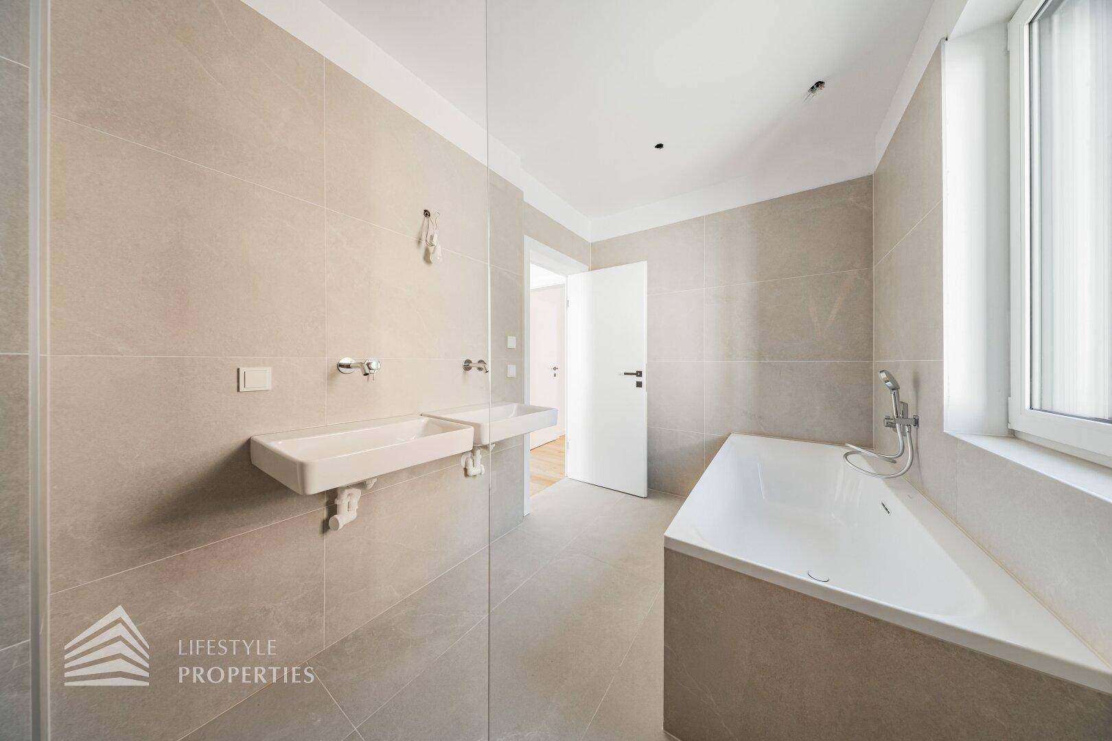 Helles Badezimmer mit modernen Fliesen, Badewanne und zwei Waschbecken.