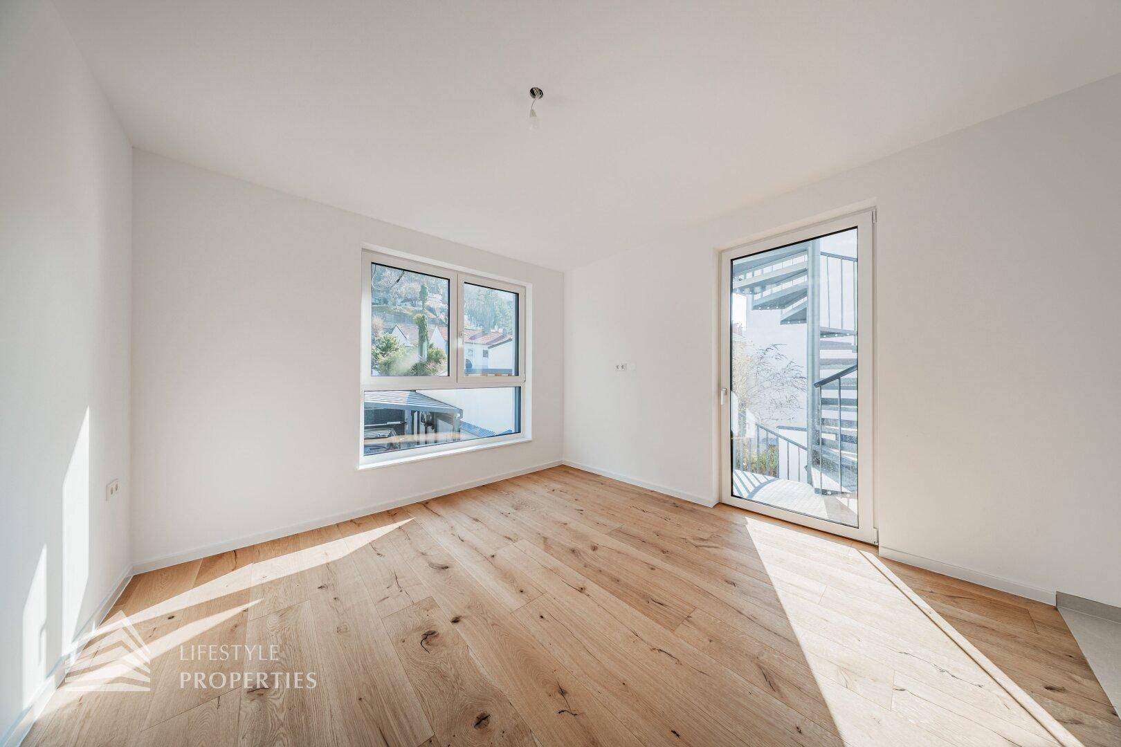 Helles Schlafzimmer mit Holzdielenboden und Zugang zu einem Balkon über eine Wendeltreppe.