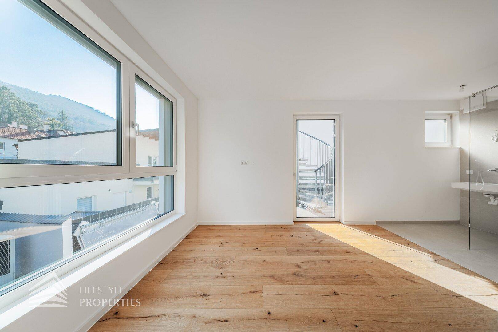Großes Schlafzimmer mit Holzdielenboden und offenem Badbereich mit Dusche und Waschbecken.