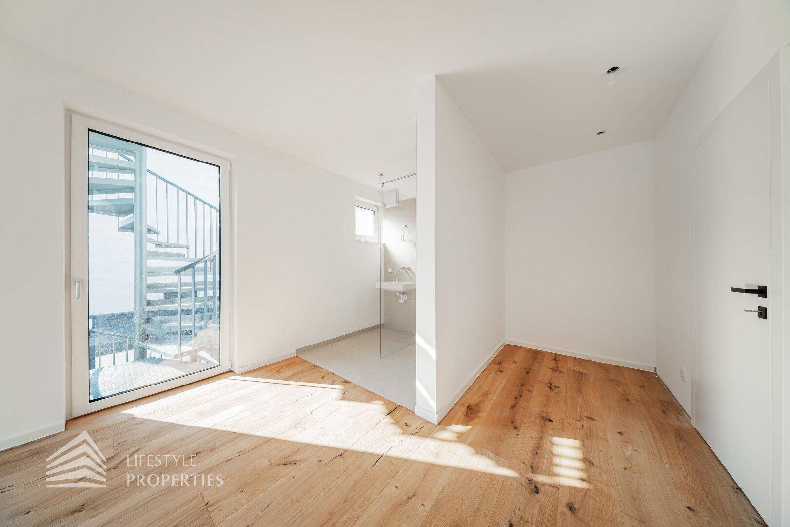 Schlafzimmer mit Holzdielenboden und integriertem Badbereich, der viel Licht erhält.