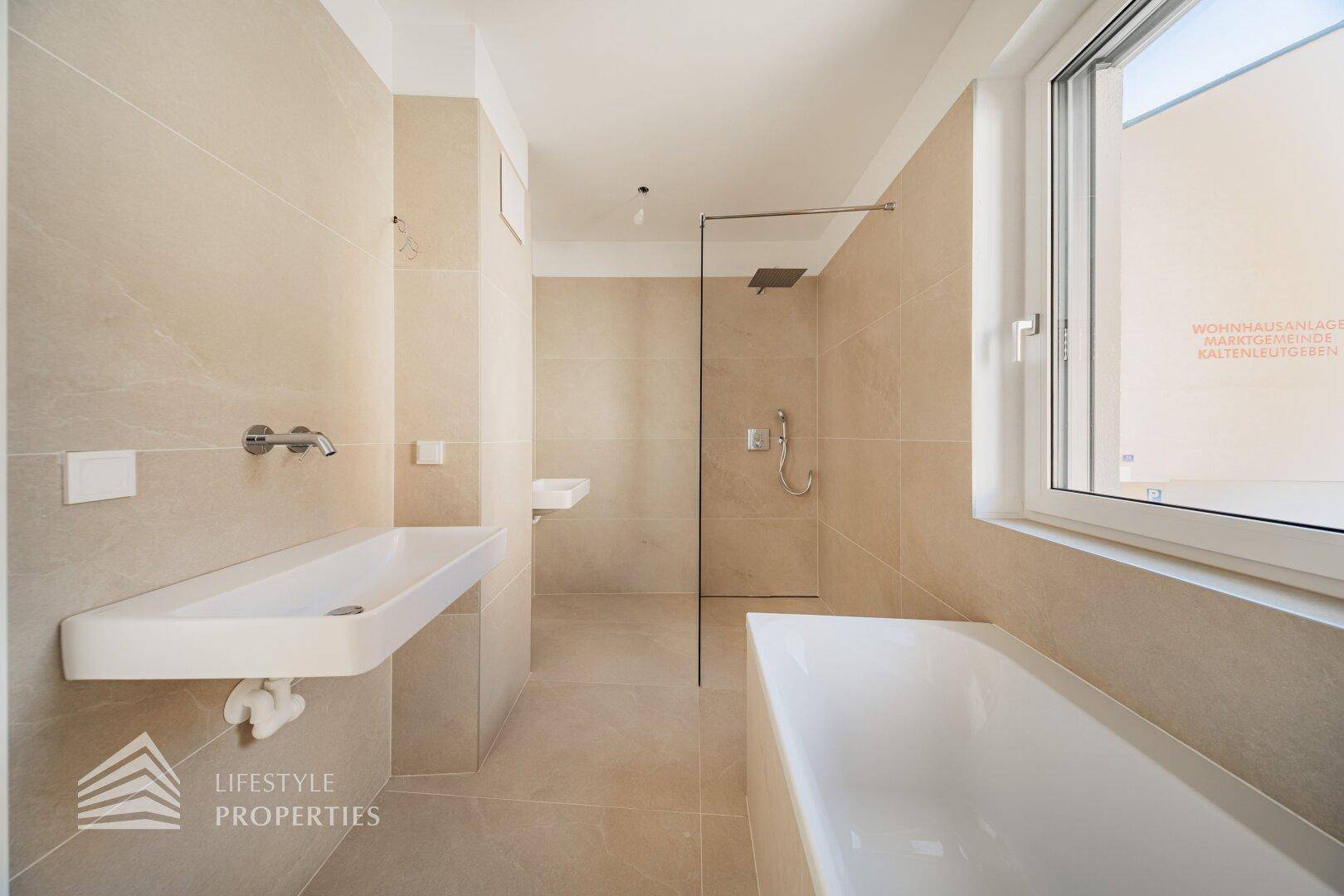 Elegantes Badezimmer mit beigefarbenen Fliesen, Badewanne, bodengleicher Dusche und zwei Waschbecken.