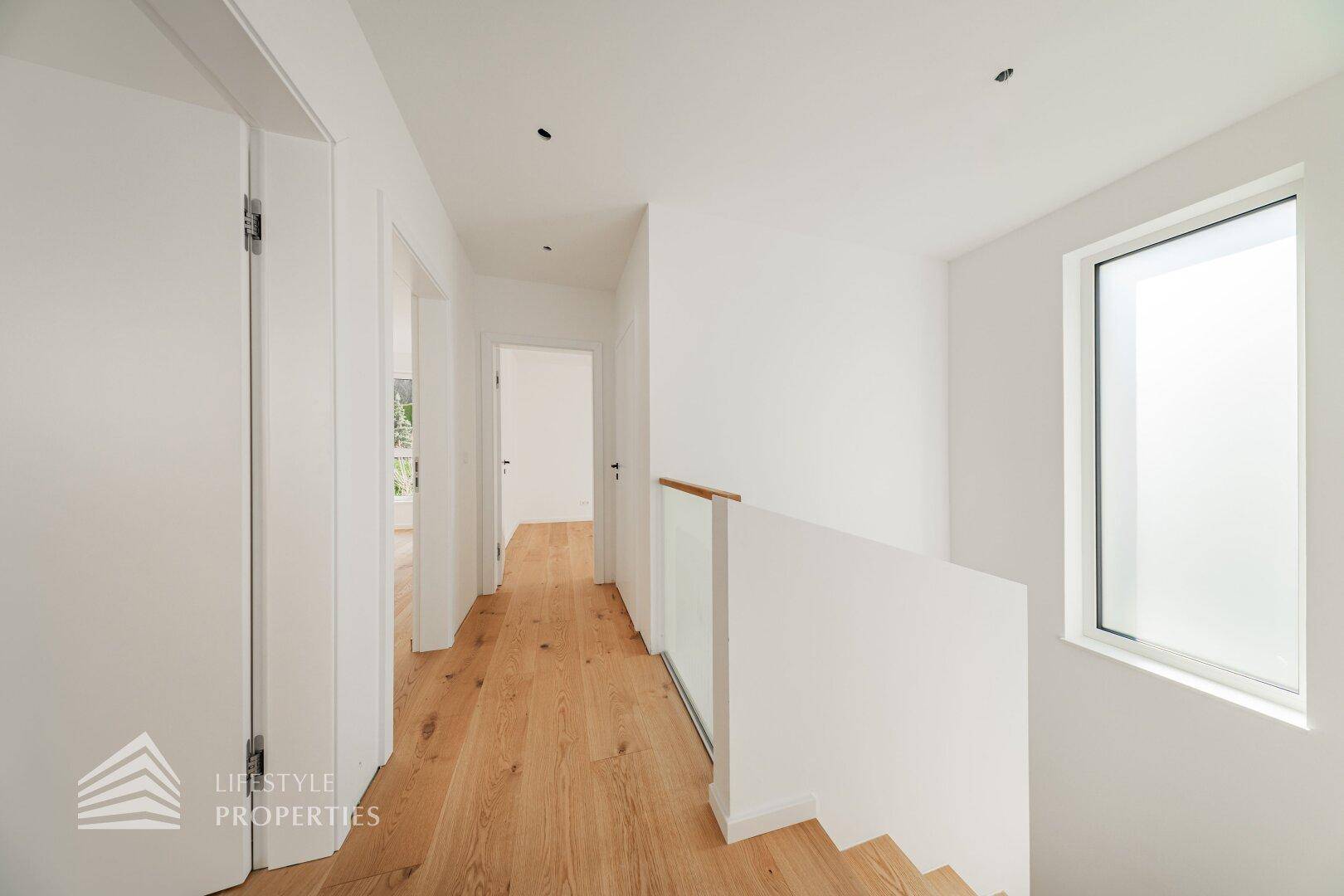Heller Flur im Obergeschoss mit Holzboden und moderner Glasbrüstung an der Treppe.