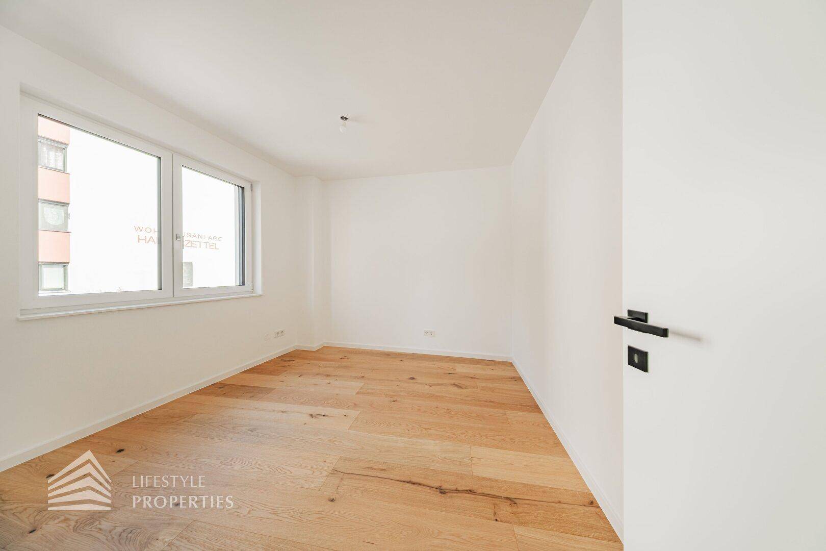 Leeres Schlafzimmer mit Holzboden und großen Fenstern, die viel natürliches Licht hereinlassen.