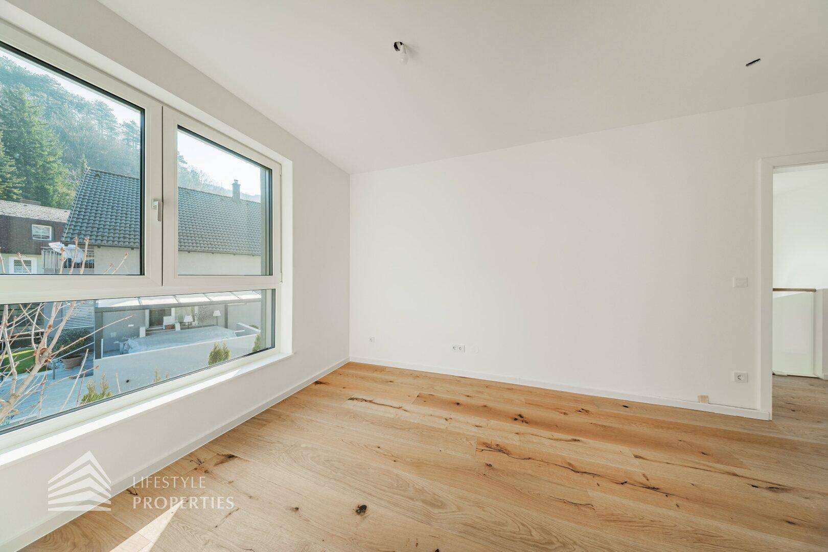 Heller Raum mit Holzboden und großen Fenstern, die einen Blick auf die Umgebung bieten.