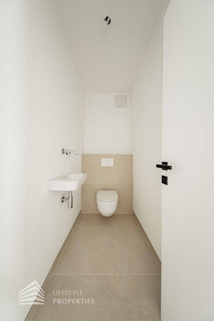 Schlichtes Gäste-WC mit wandmontierter Toilette und kleinem Waschbecken.