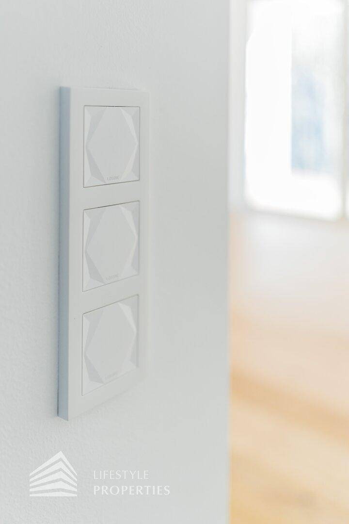 Modernes Lichtschalter-Panel mit drei stilvollen Tasten an einer weißen Wand.