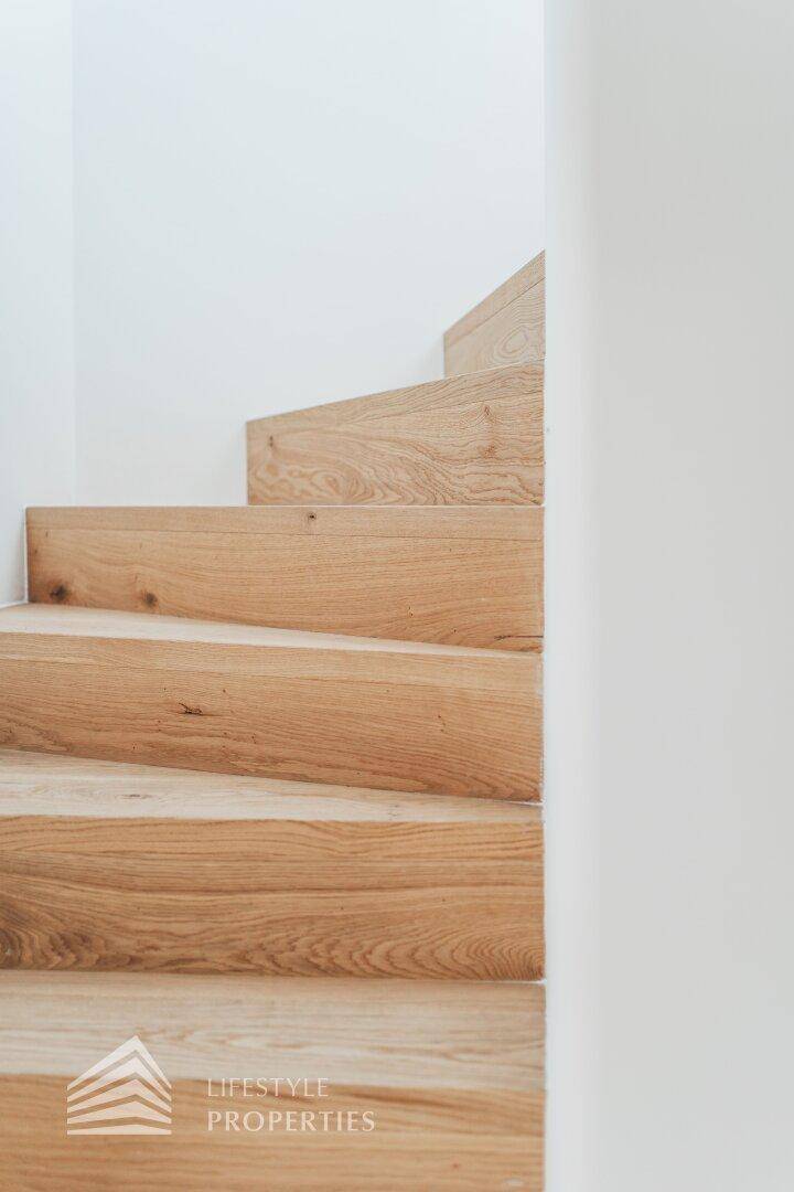 Moderne Holztreppe mit klaren Linien und weiß gestrichenen Wänden.