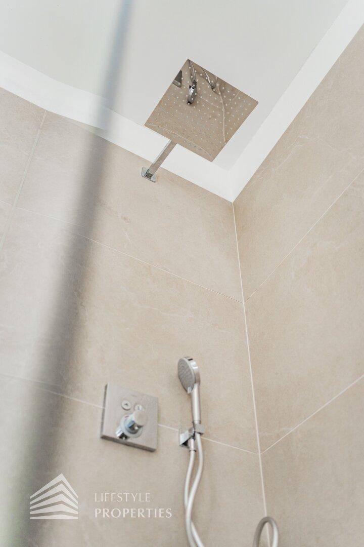 Hochwertige Regendusche und Handbrause in einem modern gefliesten Badezimmer.