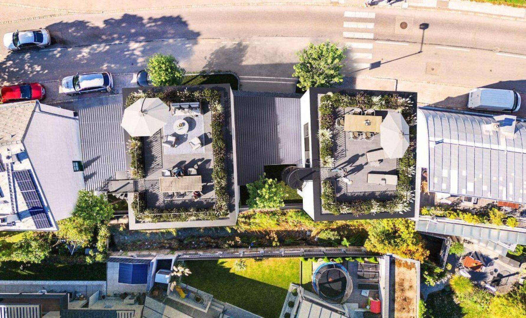 Senkrechte Luftaufnahme der beiden modernen Gebäude mit möblierten Dachterrassen und Sonnenschirmen.
