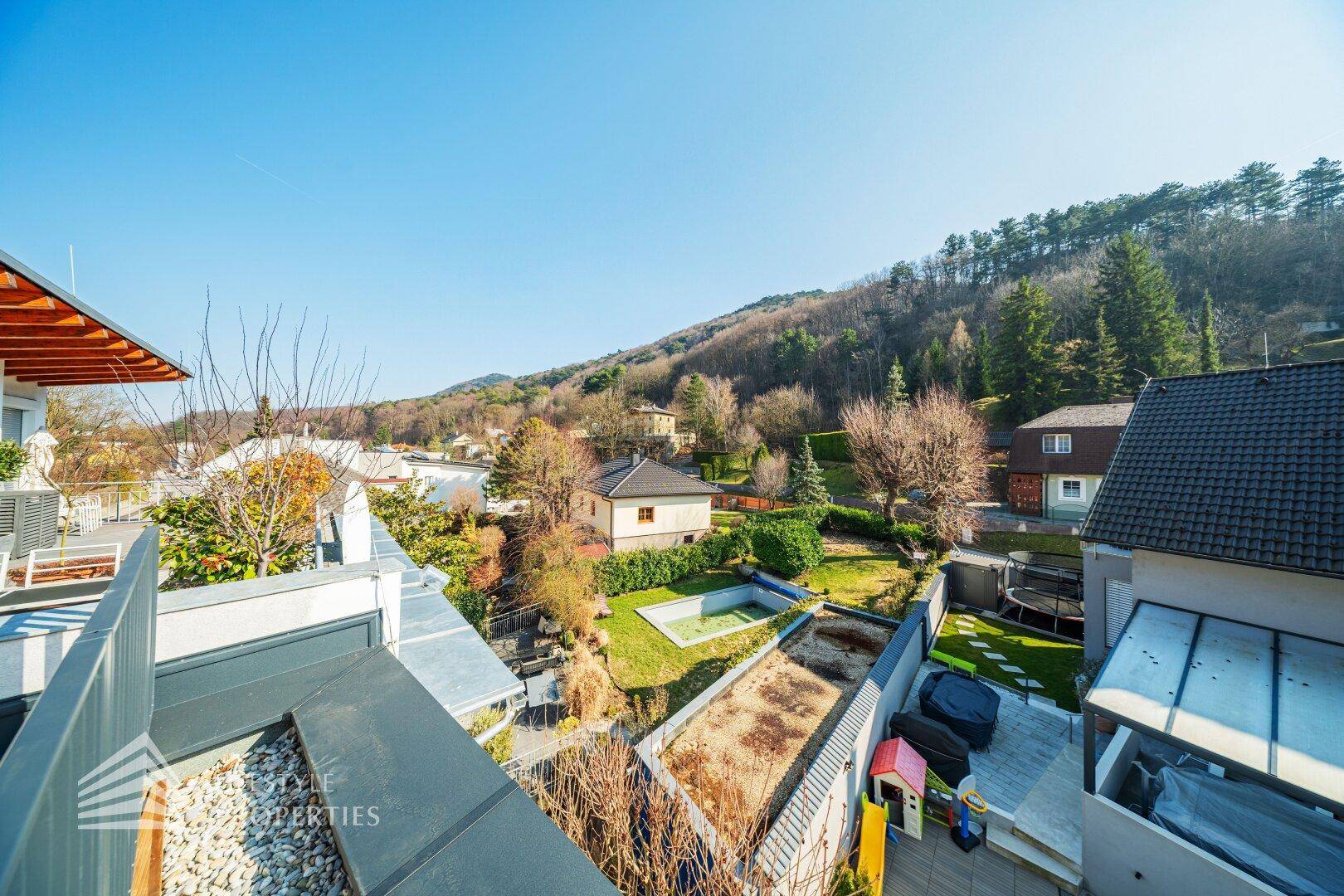 Blick von einem Balkon auf grüne Gärten und die hügelige Landschaft in der Ferne.
