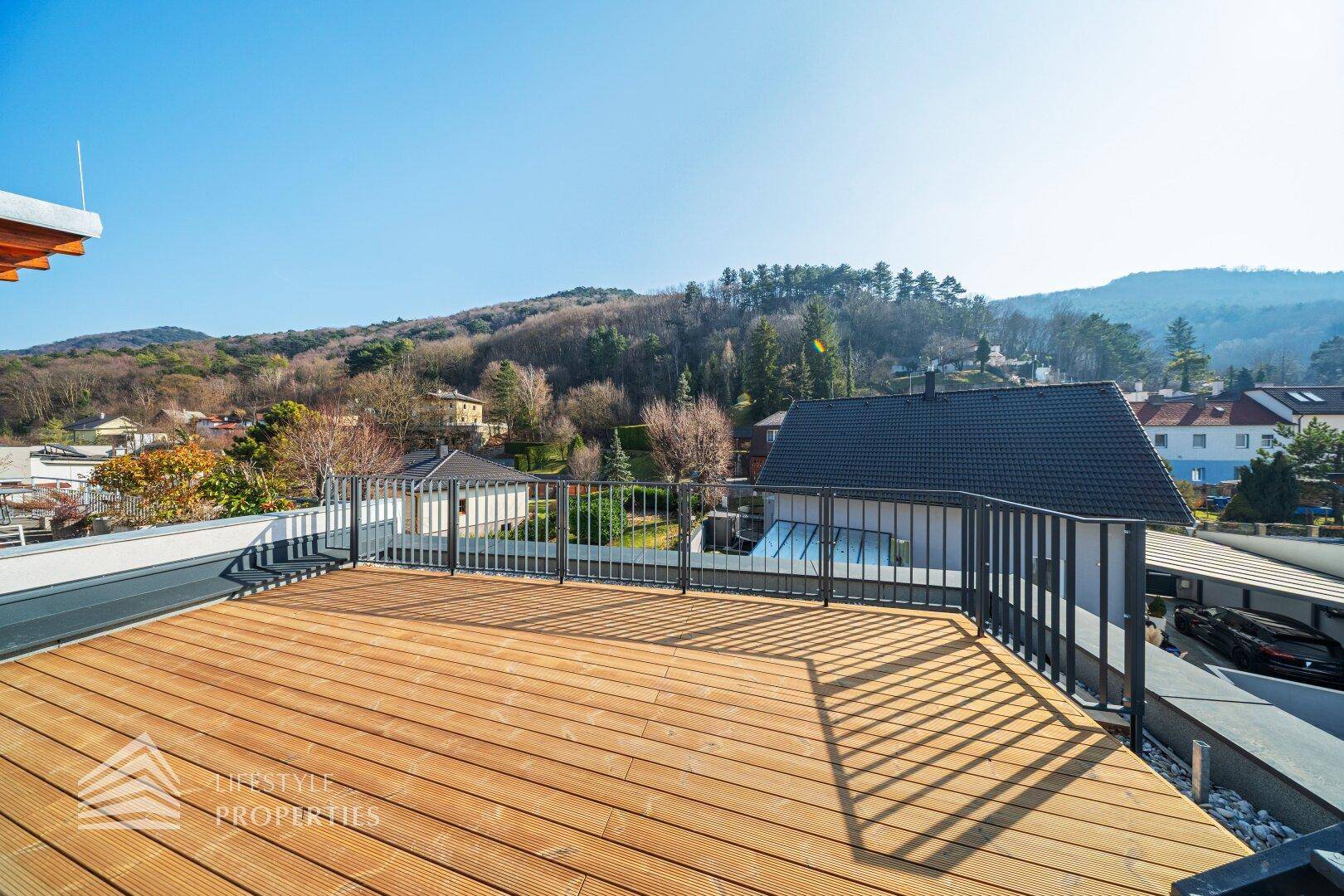Geräumige Dachterrasse mit Holzdielen und Panoramablick über die Wohngegend und Berge.