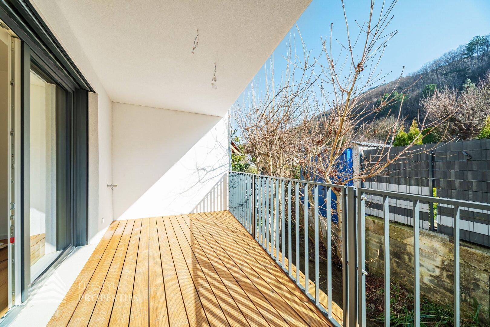 Langer, schmaler Balkon mit Holzboden und Metallgeländer, bietet Blick auf Bäume und Hügel.