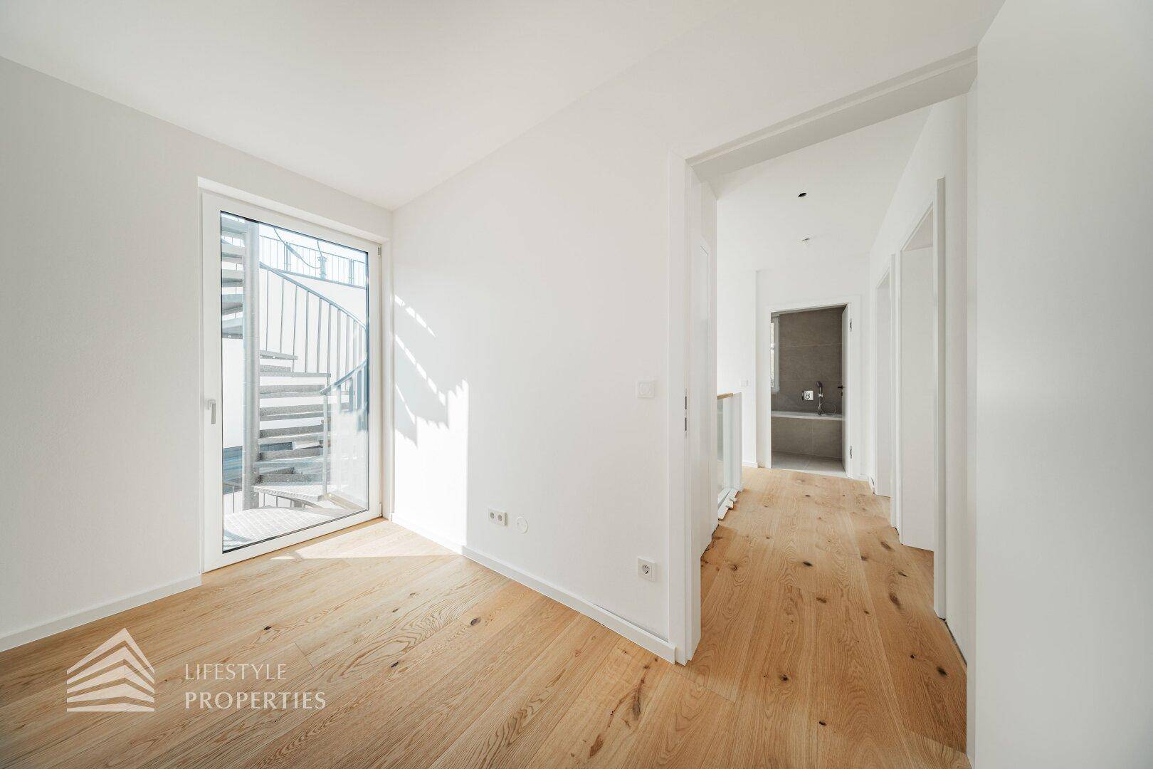 Heller Raum mit Holzboden und Zugang zu einer Außentreppe, mit Blick in ein Badezimmer.
