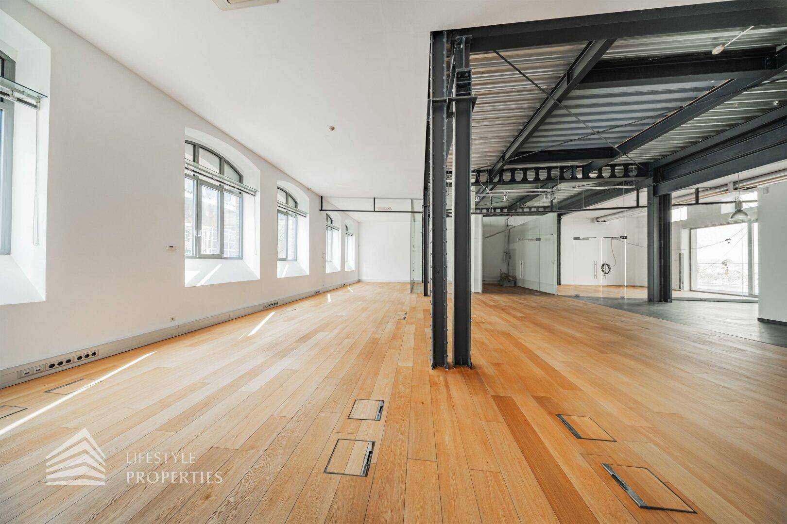 Heller Büroraum mit Holzboden und hohen Fenstern, die eine angenehme Arbeitsatmosphäre schaffen.