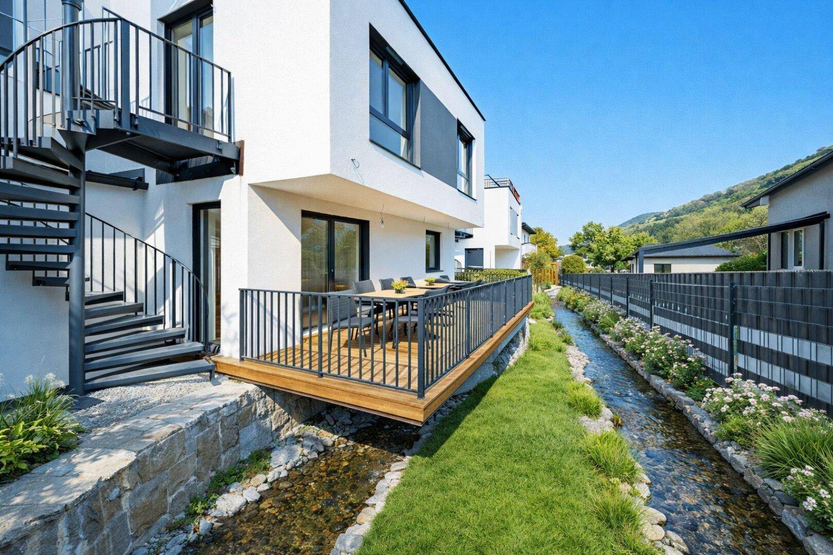 Moderne Terrasse mit Holzboden und Geländer, direkt an einem kleinen Bach gelegen, mit Blick auf die Natur.