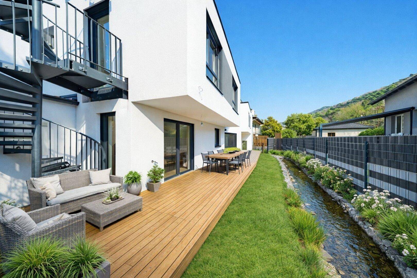 Geräumige Holzterrasse mit Lounge-Möbeln und Essbereich, direkt am kleinen Bach gelegen.