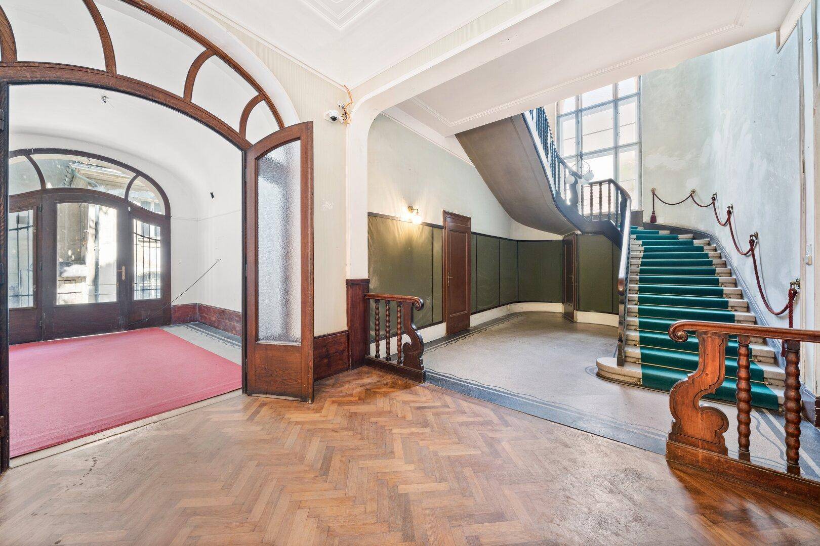 Repräsentativer Eingangsbereich mit Holzparkett und geschwungener Treppe mit grünem Teppich.