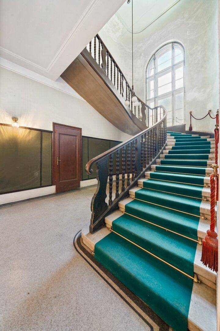 Elegantes Treppenhaus mit grünem Teppich, Holzgeländer und großem Bogenfenster.